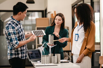 Diverse team with Asian man, African American woman, Caucasian woman discussing a clean energy city planning project with building models and solar panels.