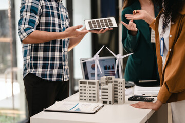 Diverse team with Asian man, African American woman, Caucasian woman discussing a clean energy city planning project with building models and solar panels.