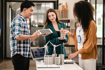 Diverse team with Asian man, African American woman, Caucasian woman discussing a clean energy city planning project with building models and solar panels.