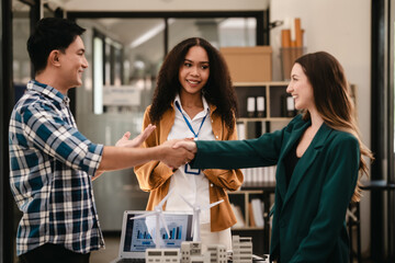 Obraz premium Diverse team with Asian man, African American woman, Caucasian woman discussing a clean energy city planning project with building models and solar panels. Shaking hands