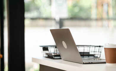 silver laptop on a desk with a blurred background. Nearby are two takeaway coffee cups and a wire basket.