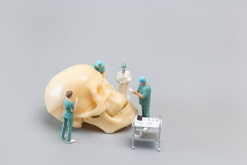 Miniature people Doctor with a giant human skull on a grey background