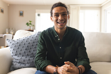 Happy biracial man with long curly hair having video call and laughing in sunny living room at home