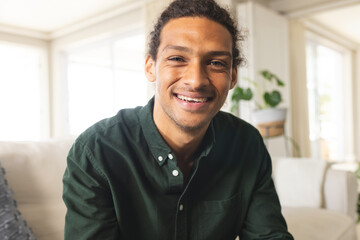 Obraz premium Happy biracial man with long curly hair having video call and smiling in sunny living room at home