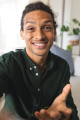 Happy biracial man with long curly hair having video call and smiling in sunny living room at home