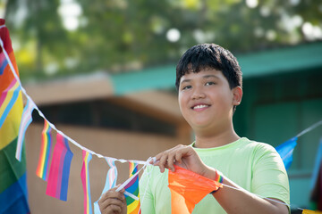 Asian boys are holding rainbow flags and wire rainbow flags which hanging around tree branches to...