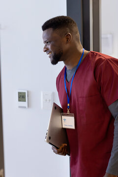 Happy african american male doctor with laptop entering into hospital room
