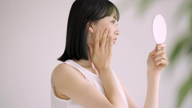 鏡で肌をチェックする白い服の若い女性