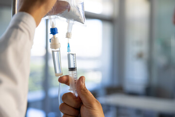 Hands of biracial male doctor preparing drip in sunny hospital room