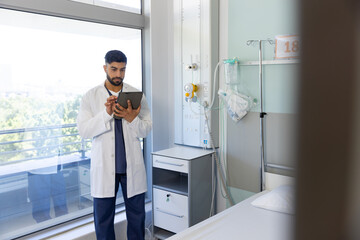 Biracial male doctor using tablet in sunny hospital room