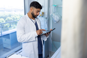 Naklejka na ściany i meble Biracial male doctor using tablet in sunny hospital room