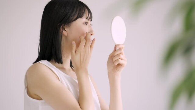 鏡で肌をチェックする白い服の若い女性