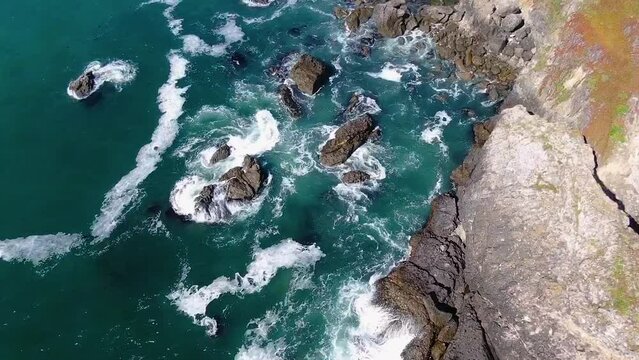 Aerial top-view video capturing the beauty of a blue rocky coast with waves gently crashing against a rugged shoreline in Bodega Bay, Gualala Coast California