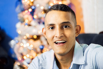 Portrait of latin american man behind a Christmas tree.