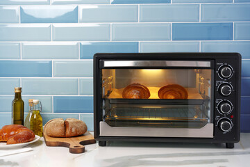 Modern mini electric oven with freshly baked croissants in kitchen - obrazy, fototapety, plakaty