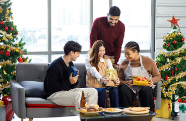 Millennial Asian Indian multinational cheerful male female friends celebrate Christmas Eve and Happy New Year holding showing presents gifts boxes in living room full decoration with Xmas tree