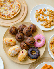 Top view closeup shot of delicious tasty yummy fast foods donuts cupcake pizza and fried chicken on wooden tray and white dish placed on table for group party celebrating Christmas eve and New Year