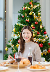 Asian cheerful female smiling eating delicious tasty foods donut cupcake pizza together in dining room fully decorated with Xmas tree celebrated Christmas Eve festive.