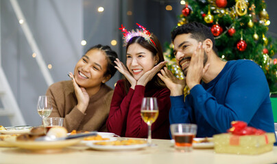 Group of Asian Indian happy cheerful male female friends wears reindeer antlers headband happy meeting with champagne beverage glasses together on dinner table celebrating Christmas eve in dining room