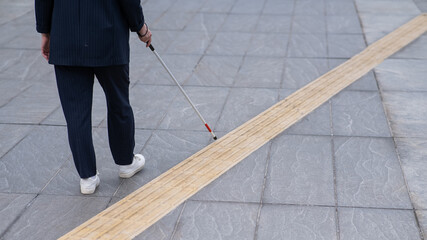 Close-up of the legs of a blind businesswoman walking along a tactile tile with a cane. 