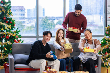 Millennial Asian Indian multinational cheerful male female friends celebrate Christmas Eve and Happy New Year holding showing presents gifts boxes in living room full decoration with Xmas tree