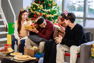 Millennial Asian Indian multinational cheerful male female friends celebrate Christmas Eve and Happy New Year holding showing presents gifts boxes in living room full decoration with Xmas tree