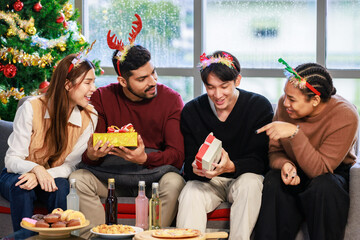 Millennial Asian Indian multinational cheerful male female friends celebrate Christmas Eve and Happy New Year holding showing presents gifts boxes in living room full decoration with Xmas tree