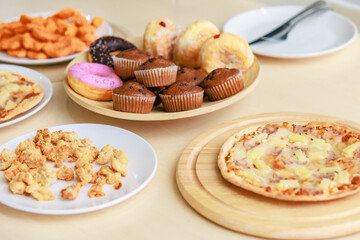 Top view closeup shot of delicious tasty yummy fast foods donuts cupcake pizza and fried chicken on wooden tray and white dish placed on table for group party celebrating Christmas eve and New Year