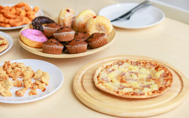 Top view closeup shot of delicious tasty yummy fast foods donuts cupcake pizza and fried chicken on wooden tray and white dish placed on table for group party celebrating Christmas eve and New Year