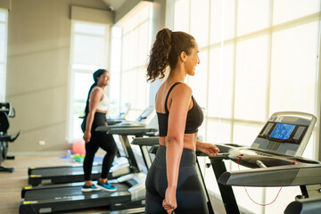 Fototapeta premium Fitness exercising in gym. Sporty woman in a sports bra doing exercise by running on treadmill during a workout at the gym fitness center with group of people.