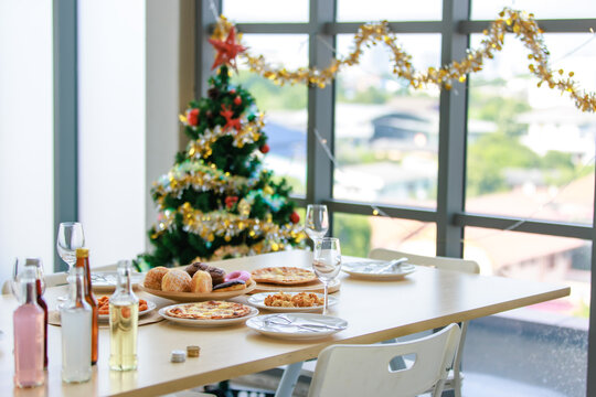 Delicious tasty fast foods snacks donut cupcake pizza in wood tray and white dishes placed on table in dining room full decorated with Xmas tree celebrating Christmas Eve and Happy New Year festival