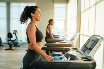 Fitness exercising in gym. Sporty woman in a sports bra doing exercise by running on treadmill...