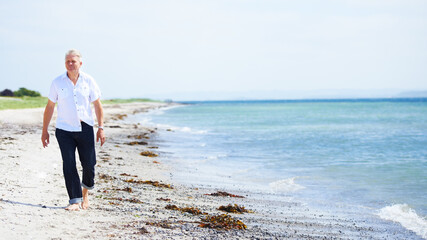 Beach, walking and senior man on a travel tropical vacation, holiday or weekend trip in summer. Adventure, outdoor and elderly male person in retirement on the sand by the ocean or sea on getaway.