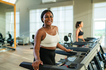 Fitness exercising in gym. Sporty woman in a sports bra doing exercise by running on treadmill during a workout at the gym fitness center with group of people. - obrazy, fototapety, plakaty