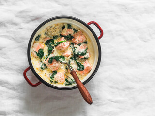 Salmon, cream, spinach sauce stew in a saucepan on a light background, top view