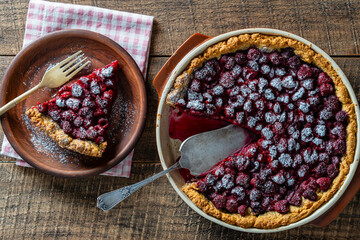 Raspberry pie in a ceramic dish on wooden background, closeup, top view