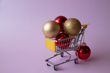 Christmas balls, toys in mini trolley from supermarket on pink background