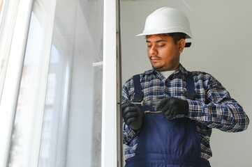 Indian Workman in overalls installing or adjusting plastic windows in the living room at home
