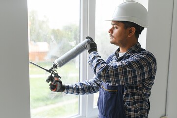 Indian worker using a silicone tube for repairing of window indoor