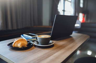 Close-up shot, coffree cup with computer laptop and bread on wooden table in cafe. people start working in the morning with breakfast