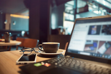 Close-up shot, coffree cup with computer laptop, eyeglasses and smart phone on wooden table in...