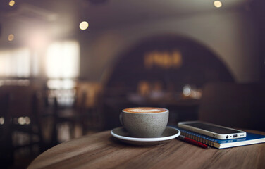 Close-up shot, coffree cup with smart phone placed on a notebook on wooden table in cafe. Vintage light, blurred background