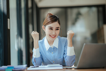 Happy beautiful Asian businesswoman holding money in hand Smartphone and laptop on table in office...