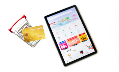 Top view, credit card in small supermarket cart with tablet computer. defocus on screen show website for shopping. Online shopping and home shopping concept, white background