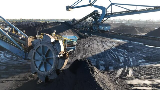 Industrial coal mine with conveyor belts and large wheel excavator. Aerial tracking shot of coal shipping and distribution at port.