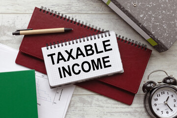 Taxable Income text on a notebook on a diary. a table clock