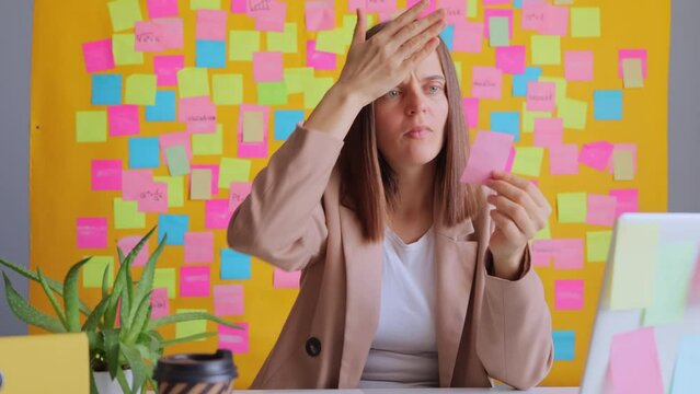 Table workplace. Work manager. Notebook planning. Shocked woman working on laptop computer at her workplace with multicolored memo cards forgot about important task making facepalm gesture.