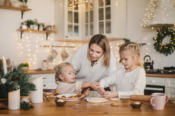 mother and two daughters prepare homemade Christmas gingerbread in the kitchen decorated for the New Year. Traditional holiday cooking with the whole family. Toned defocused noise vintage image