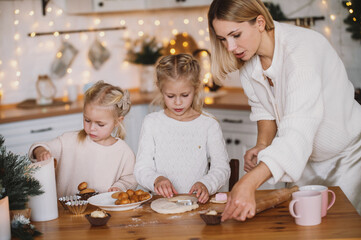 mother and two daughters prepare homemade Christmas gingerbread in the kitchen decorated for the New Year. Traditional holiday cooking with the whole family. Toned defocused noise vintage image