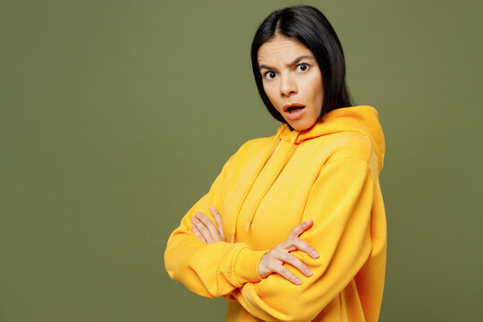 Side view young sad shocked frowning Latin woman wears yellow hoody casual clothes hold hands crossed folded look camera isolated on plain pastel green background studio portrait. Lifestyle concept.